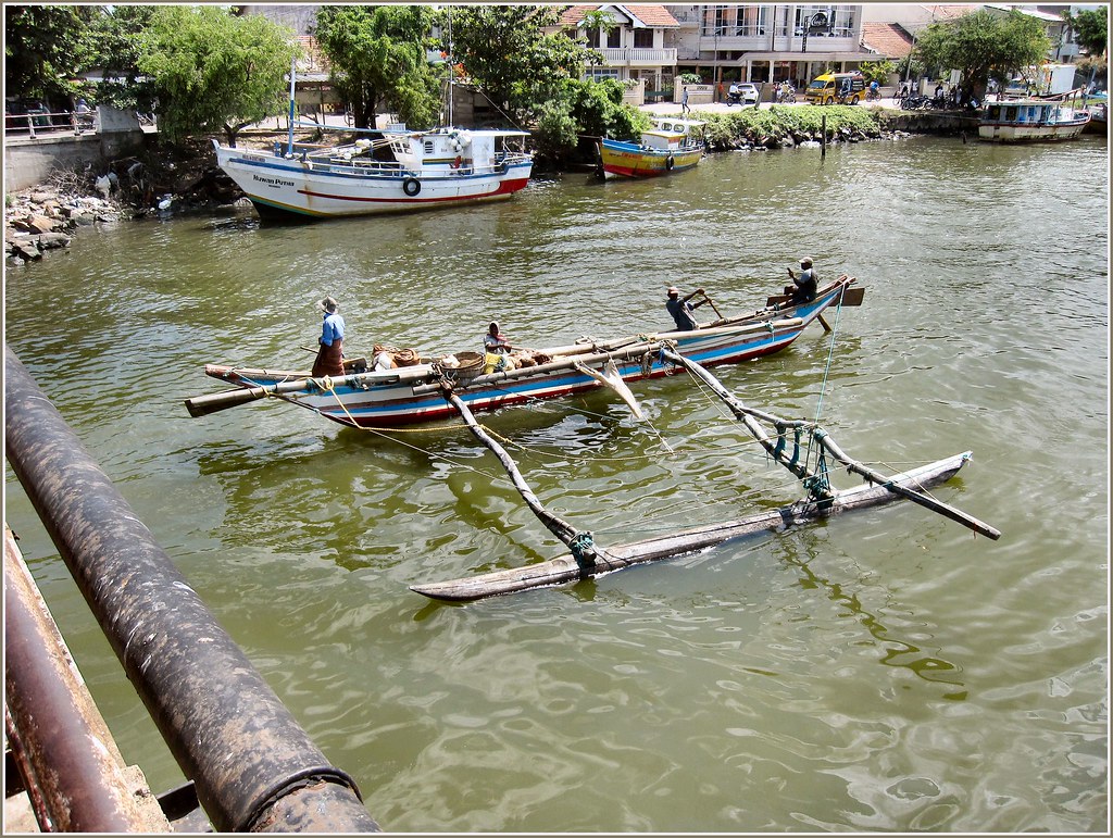 Fishermen poling an outrigger under a Negombo canal bridge